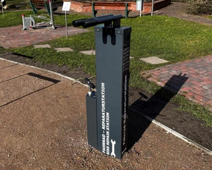 Fahrradflickstation Greetsiel Graue Fahrradreparaturstation mit Werkzeugen auf befestigtem Platz neben Rasenfläche in Greetsiel.