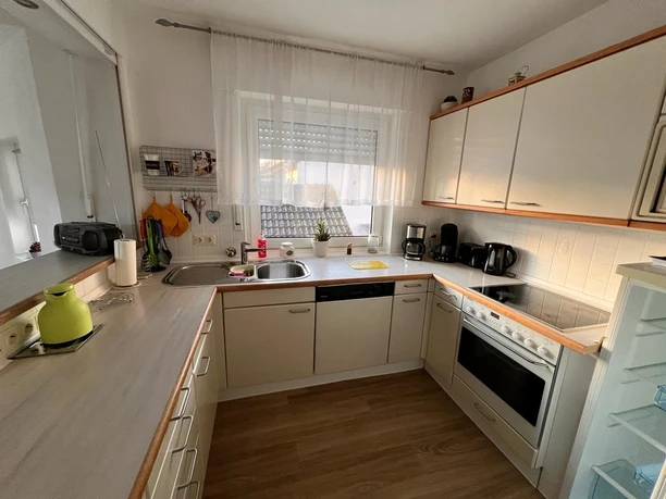 Helle Küche mit U-Form-Arbeitsfläche, Elektrogeräten, hellem Holzfußboden und Fenster.