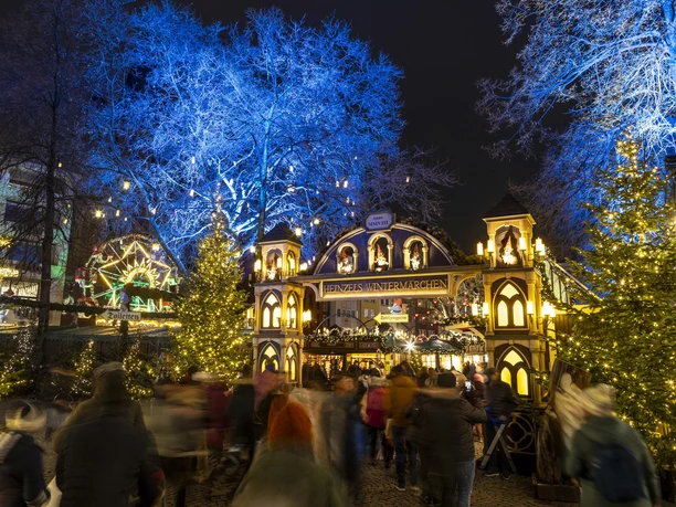 Heinzels Winter Fairytale The Christmas market on the Alter Markt in Cologne shines in a blaze of lights with festive decorations and a festive archway, framed by blue trees.