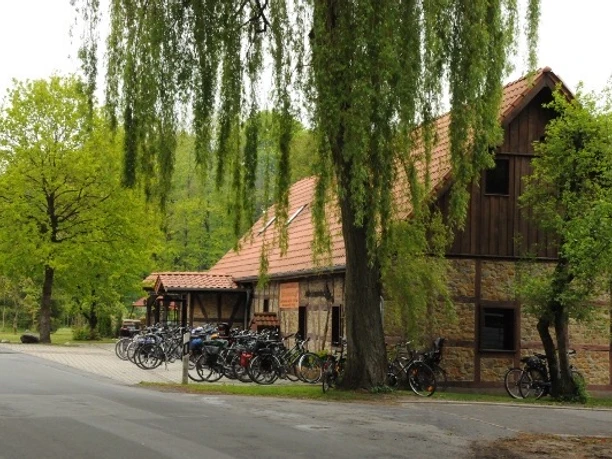 Kaffee Hexenbrink Außenansicht Ein rustikales Gebäude, umgeben von Bäumen, mit geparkten Fahrrädern an der Straßenseite.