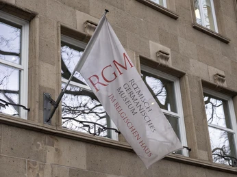 Belgian House RGM Das Bild zeigt eine elegante, cremefarbene Flagge vor der Fassade eines Gebäudes mit der Aufschrift "Römisch-Germanisches Museum im Belgischen Haus Köln". The picture shows an elegant, cream-colored flag in front of the facade of a building with the inscription "Römisch-Germanisches Museum im Belgischen Haus Köln".