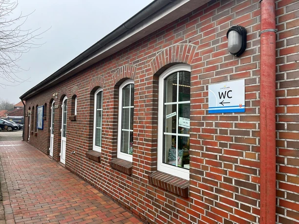 Öffentliche Toilette , neben Apen Touristik.jpeg Ziegelbau mit weißen Fenstern und Toilettenschild daneben. Perfekt für Touristen geeignet.