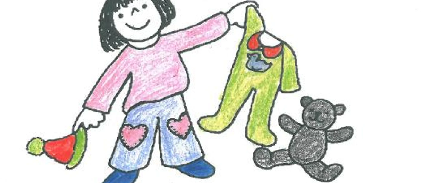 Kinder.jpg Ein lächelndes Kind hebt einen grünen Schlafanzug mit Entenmotiv neben einem sitzenden Teddybär.