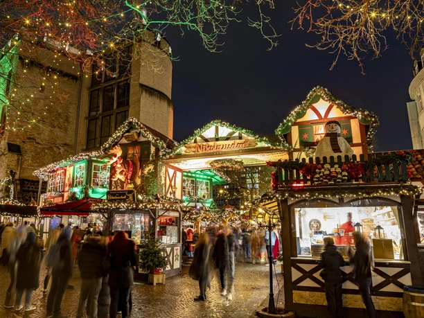 Nikolausdorf am Rudolfplatz Belebter Weihnachtsmarkt in Köln bei Nacht, geschmückte Hütten, bunte Lichter erhellen den Platz.