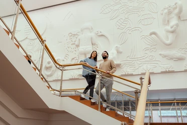 Museum Ludwig Das Bild zeigt zwei Personen, die eine Treppe im Museum Ludwig in Köln hinaufgehen, vor einer kunstvoll gestalten Wandgestaltung.