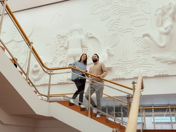 Museum Ludwig Das Bild zeigt zwei Personen, die eine Treppe im Museum Ludwig in Köln hinaufgehen, vor einer kunstvoll gestalten Wandgestaltung.The picture shows two people walking up a staircase in the Museum Ludwig in Cologne, in front of an artistically designed mural.