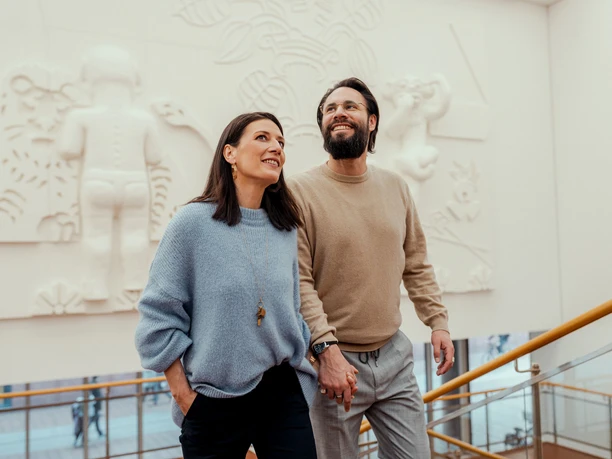 Museum Ludwig Ein Paar schreitet händchenhaltend eine breite Treppe im Museum Ludwig hinauf, umgeben von moderner Kunst an der Wand.