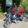Paralleltandem Modernes Elektrofahrrad mit drei Rädern und zwei Sitzen stehend auf sonnigem Radweg.