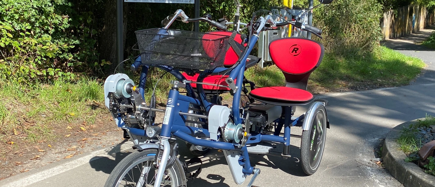 Paralleltandem Modernes Elektrofahrrad mit drei Rädern und zwei Sitzen stehend auf sonnigem Radweg.
