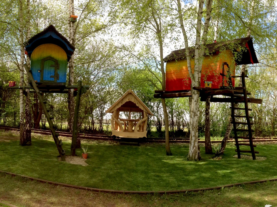 haus3_2048x1226.jpg Eine Erlebnisbahn fährt durch einen Birkenwald. Zwischen den Bäumen stehen bunte Baumhäuser.