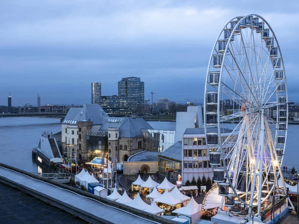 Kölner Hafen-Weihnachtsmarkt Weihnachtsmarkt vor dem Schokoladenmuseum in Köln, umrahmt vom Rheinufer und einem beleuchteten Riesenrad.