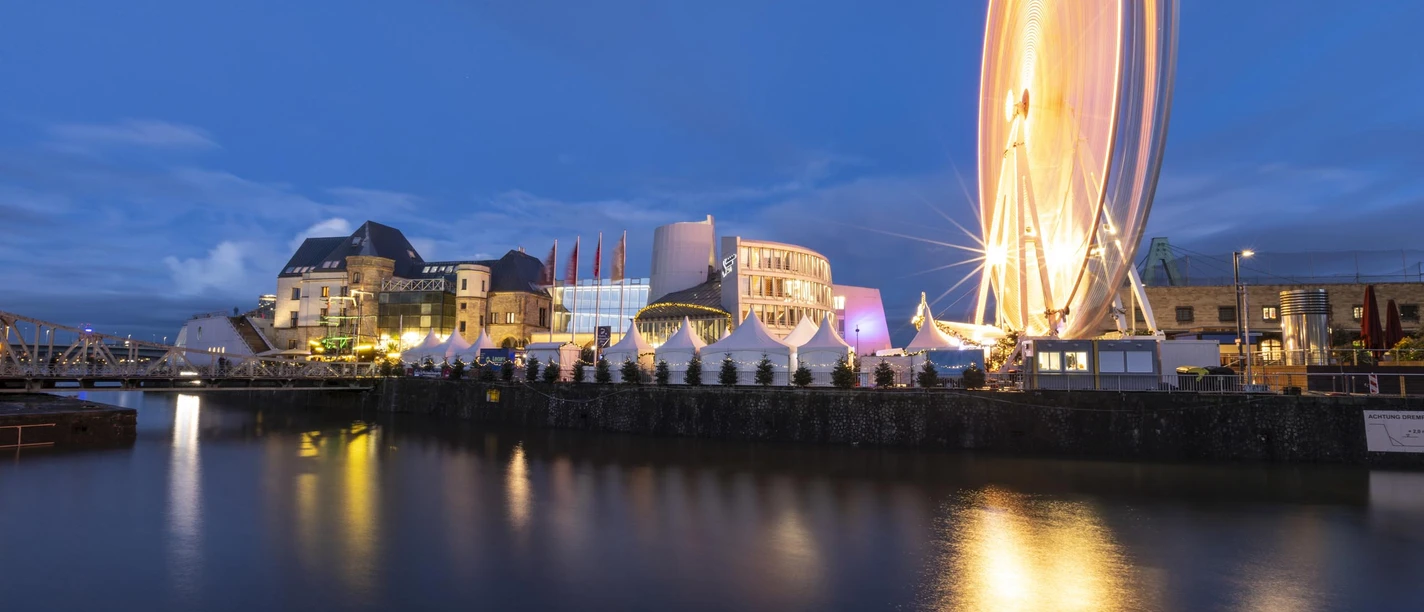 Kölner Hafen-Weihnachtsmarkt Abendstimmung am Rhein: Weihnachtsmarkt mit Lichtern, markantem Schokoladenmuseum und Riesenrad.