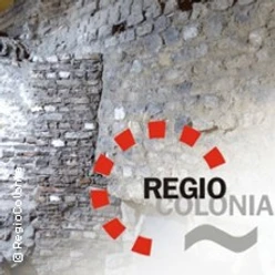 Eine Bruchsteinmauer mit dem Schriftzug "REGIO COLONIA" und einem kreisförmigen roten Logo.