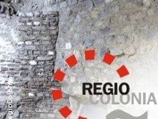 Eine Bruchsteinmauer mit dem Schriftzug "REGIO COLONIA" und einem kreisförmigen roten Logo.