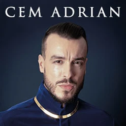 Cem Adrian blickt entschlossen in die Kamera, gekleidet in einen dunkelblauen Anzug mit goldenen Details.