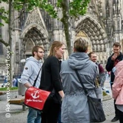 Gruppe vor gotischer Domfassade im Gespräch auf einem Platz mit Bäumen.