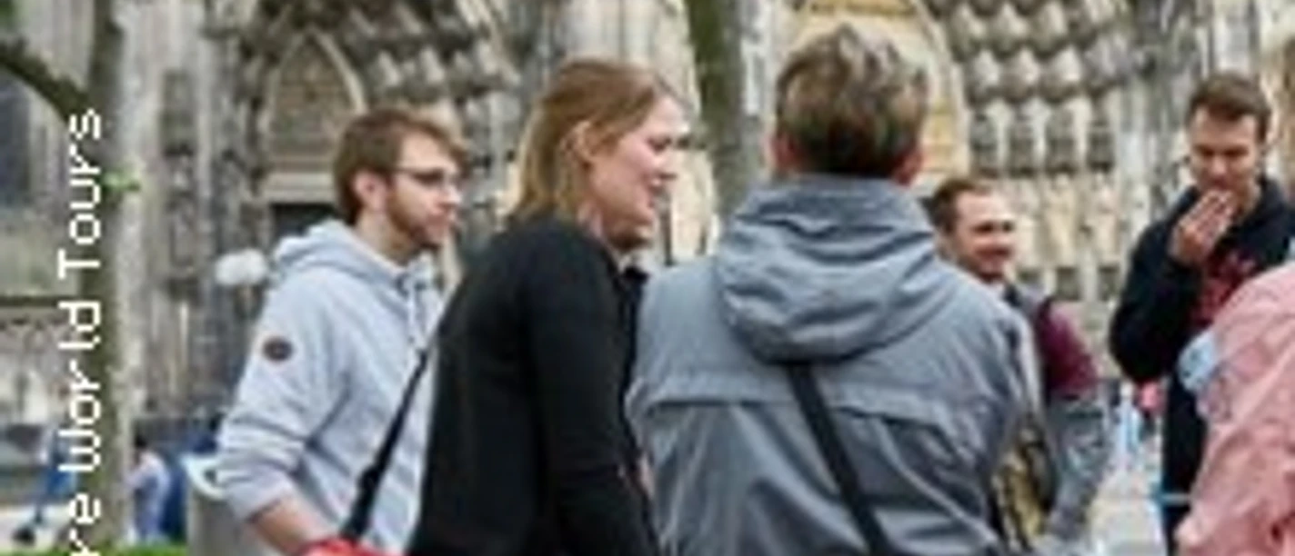 Gruppe vor gotischer Domfassade im Gespräch auf einem Platz mit Bäumen.