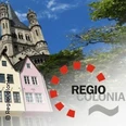 Bunte Häuser und eine große Kirche neben dem Regio-Colonia-Logo vor blauem Himmel