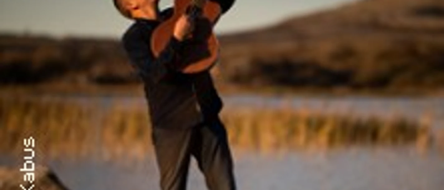 Ein Gitarrist steht am Ufer eines Gewässers und spielt leidenschaftlich in der Abenddämmerung.