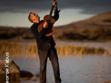 Ein Gitarrist steht am Ufer eines Gewässers und spielt leidenschaftlich in der Abenddämmerung.