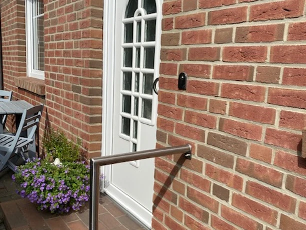 Entrance door of a brick house with white door, flower bed and handrail on the left.