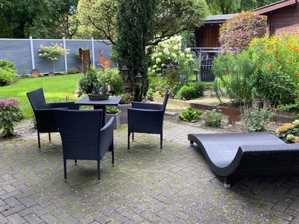 Brauer, Liebenau Gepflegte Terrasse mit modernen Rattanmöbeln, umgeben von blühenden Pflanzen und begrünten Büschen.