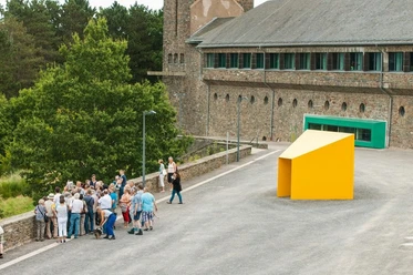 Personengruppe steht vor modernem, gelbem Kunstwerk, historische Burg Vogelsang im Hintergrund.
