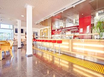 Moderne Café-Bar mit roter Theke und Hockern, hellem Interieur, Holztischen und großen Fenstern.