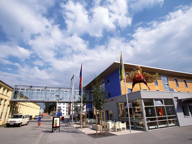 Modernes Museumsgebäude mit blauer Fassade, Glassteg und großer Skulptur davor unter blauem Himmel.