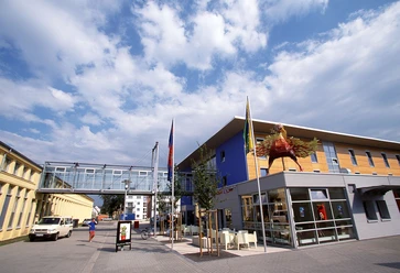 Bielefeld03.jpg Modernes Museumsgebäude mit blauer Fassade, Glassteg und großer Skulptur davor unter blauem Himmel.