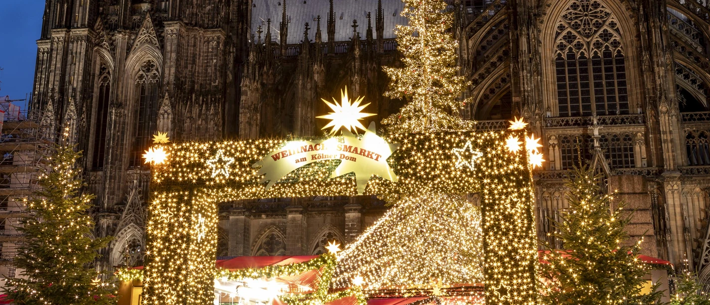 The Christmas market at Cologne Cathedral shines with bright decorations in front of the imposing cathedral backdrop.