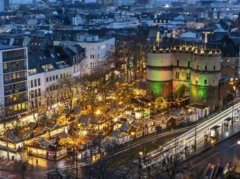 Nikolausdorf am Rudolfplatz Weihnachtsmarkt auf dem Rudolfplatz in Köln mit beleuchtetem Hahnentor in der Dämmerung.Christmas market on Rudolfplatz in Cologne with illuminated Hahnentor at dusk.