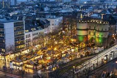 Village of St. Nicholas at Rudolfplatz Christmas market on Rudolfplatz in Cologne with illuminated Hahnentor at dusk.