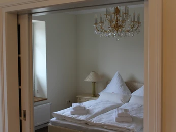 Gästehaus Rehburger Landhaus Elegantes Gästezimmer mit einem Kronleuchter, Doppelbett und Handtücher auf weißer Bettwäsche.