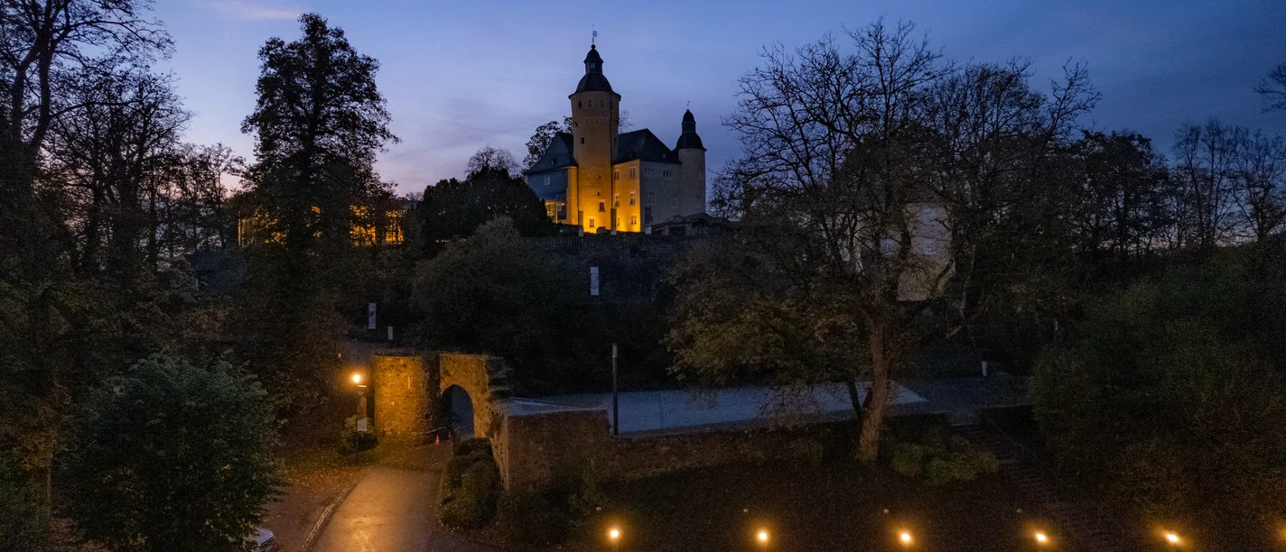 Schloss Homburg Nachtaufnahme der Burg Nümbrecht in herbstlicher Umgebung, stimmungsvoll beleuchtet, mit dunklem Himmel.