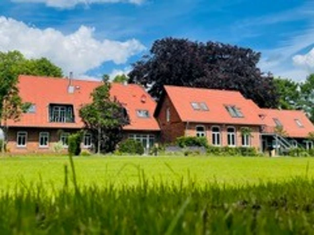 Brick buildings with red roofs and large windows in lively green surroundings under a blue sky.