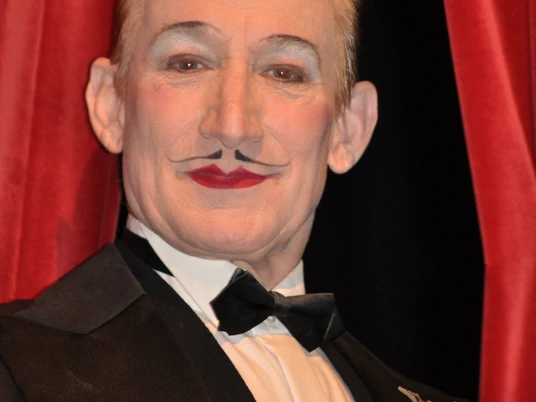 Robert Kreis.jpg Das Bild zeigt den Entertainer Robert Kreis in einem klassischen schwarzen Smoking mit Fliege vor einem roten Samtvorhang, während er lächelt.