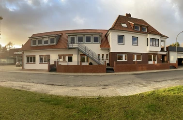 Zweigeschossiges Gebäude mit rotem Ziegeldach, weißen Fassaden und Außentreppe bei Abendlicht