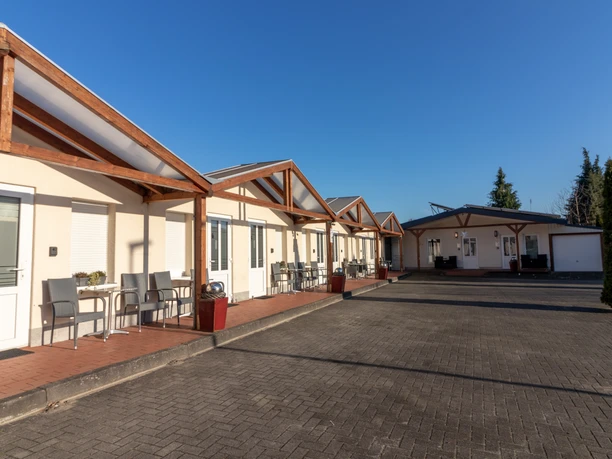 Motel Am Bürgerpark, Wehmer Str.35, Werlte.jpg Ein einstöckiges Motelgebäude mit Holzvordächern, Außenbestuhlung und gepflastertem Vorplatz.