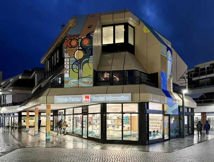 Tourist Information Paderborn mit leuchtendem Eingang in moderner Architektur bei Dämmerung.