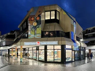 Tourist Information Paderborn, Außenansicht Tourist Information Paderborn mit leuchtendem Eingang in moderner Architektur bei Dämmerung.