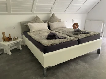 Schlafzimmer Doppelbett mit grauer Bettwäsche in einem Dachzimmer, Dachschräge mit Holzverkleidung und Dekokissen.