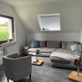 Wohnzimmer Wohnzimmer mit grauem Sofa, Sessel, Couchtischen; durch Fenster Blick auf ein grünes Feld.