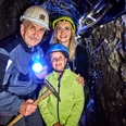 Kinderführung im Marie Louise Stolln Drei Personen mit Helmen im dunklen Bergwerksstollen, eine trägt eine Taschenlampe und lächelt.Three people with helmets in the dark mine tunnel, one of them is carrying a flashlight and smiling.Tři lidé s helmami v temném důlním tunelu, jeden z nich nese baterku a usmívá se.Trzy osoby w kaskach w ciemnym tunelu kopalni, jedna z nich niesie latarkę i uśmiecha się.Drie mensen met helmen in de donkere mijntunnel, een van hen draagt een fakkel en glimlacht.Tre persone con il casco nel buio tunnel della miniera, una di loro porta una torcia e sorride.