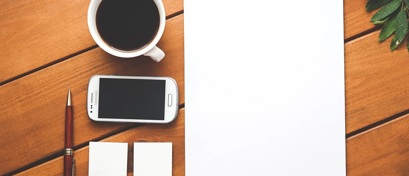 Seminar Kaffeetasse, Handy, Stift, leeres Papier und Visitenkarten auf Holztisch.