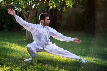 Tai-Chi Mann in weißem Tai-Chi-Anzug führt im Freien eine Tai-Chi-Position aus.