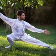 Tai-Chi Mann in weißem Tai-Chi-Anzug führt im Freien eine Tai-Chi-Position aus.