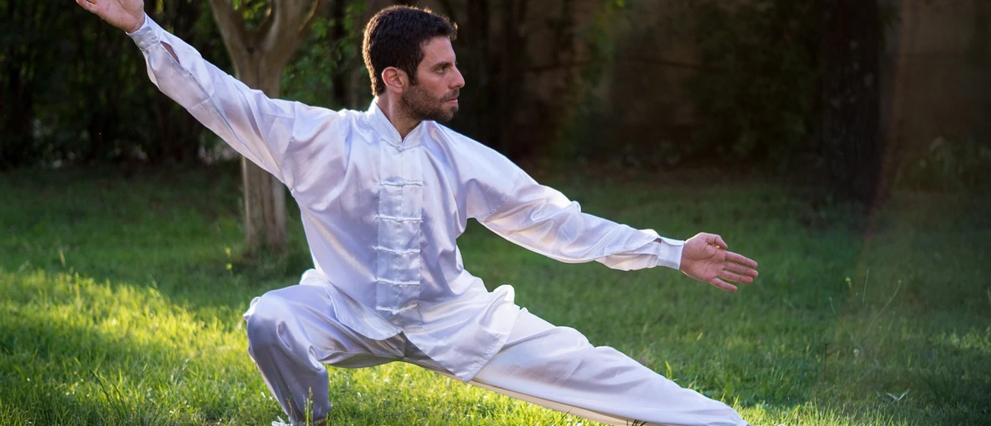 Tai-Chi Mann in weißem Tai-Chi-Anzug führt im Freien eine Tai-Chi-Position aus.