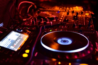 Dance Basics Kurs DJ-Pult mit Plattenspielern und Mischpult im schummrigen Rotlicht einer Clubatmosphäre.