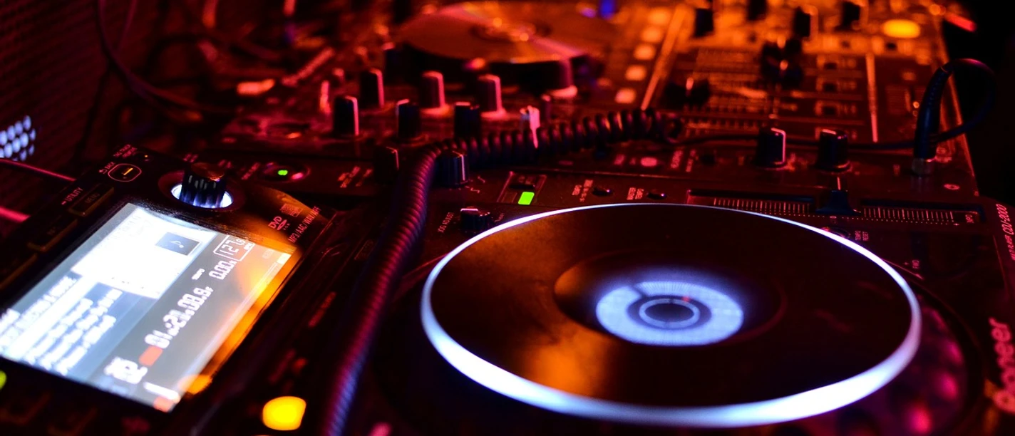 Dance Basics Kurs DJ-Pult mit Plattenspielern und Mischpult im schummrigen Rotlicht einer Clubatmosphäre.